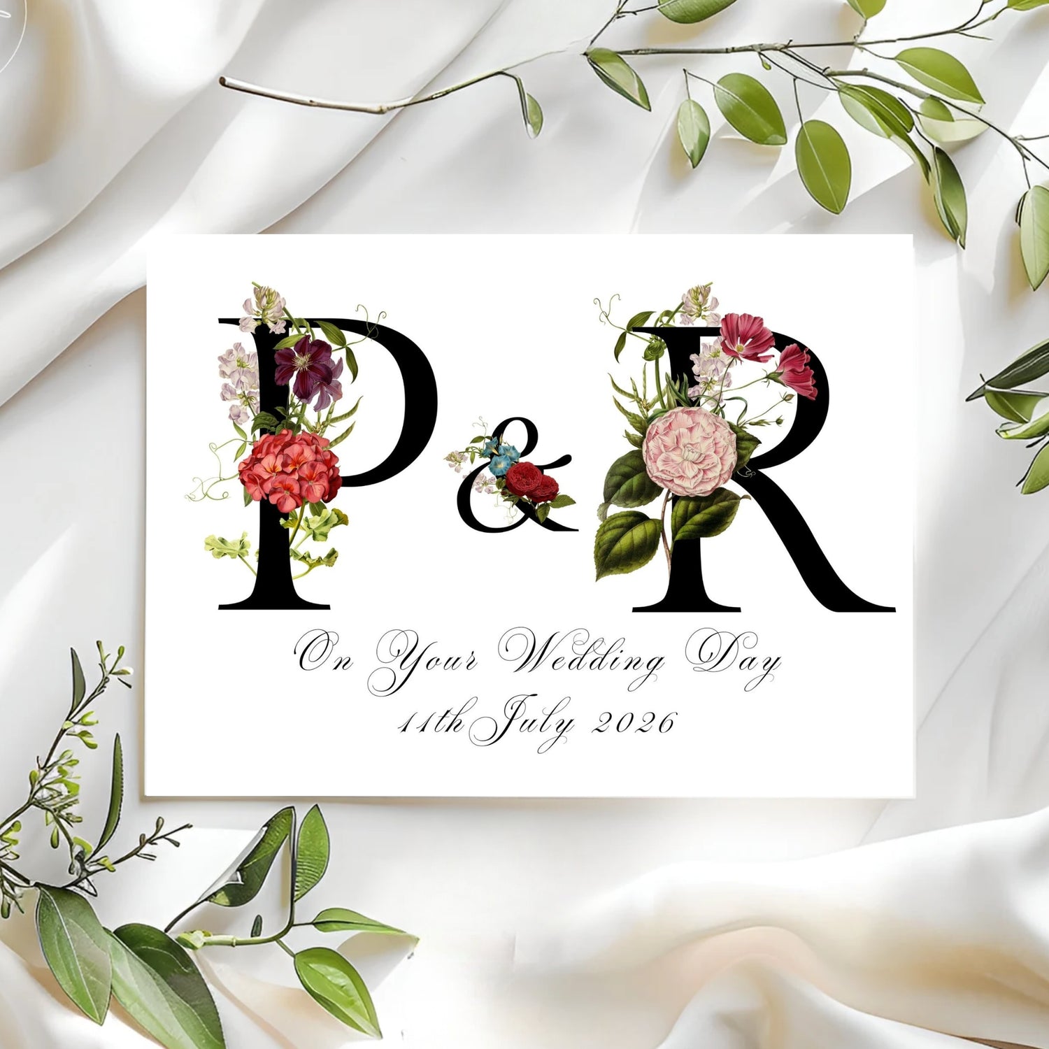 Wedding card with floral initials and date on a white fabric background