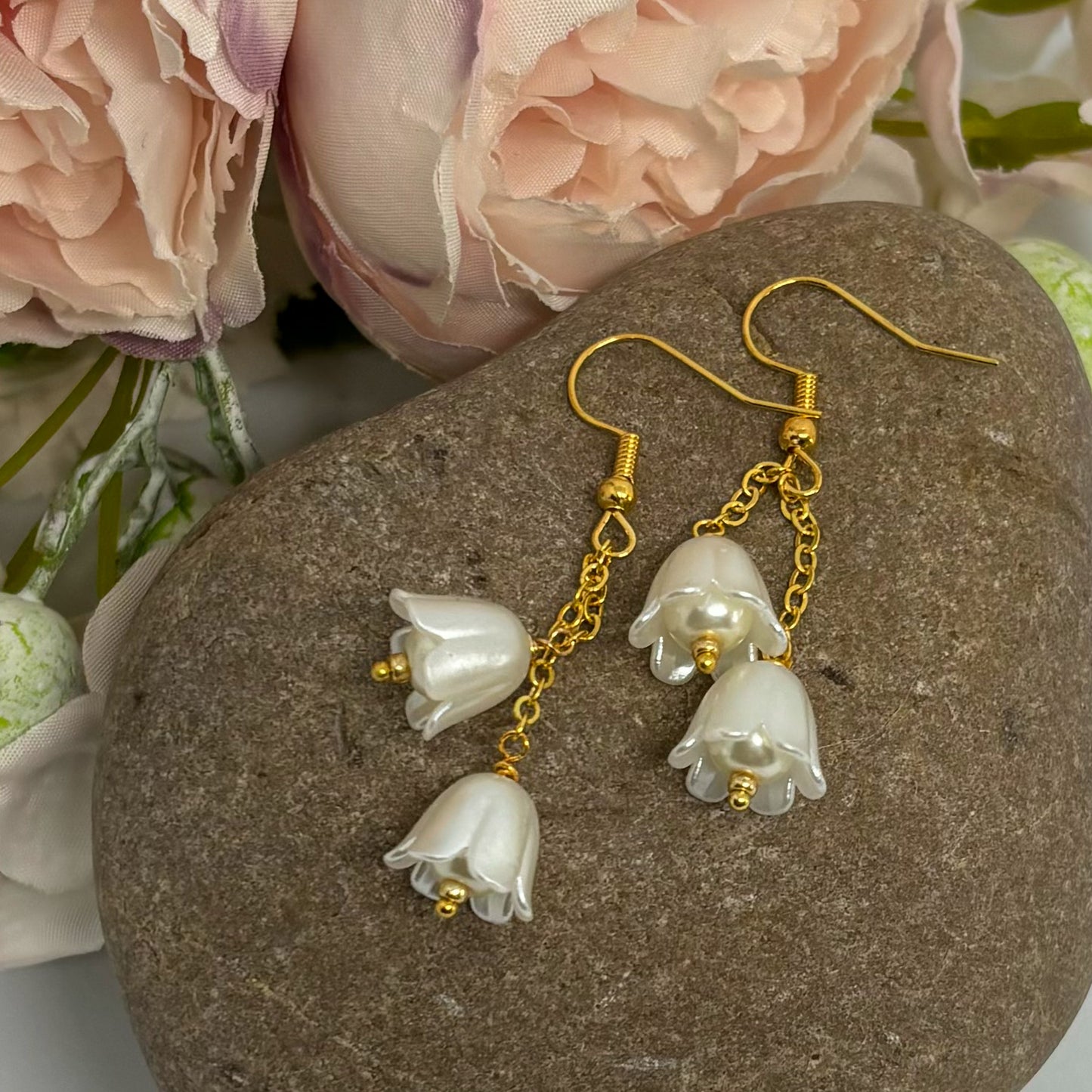 Ivory tulip earrings with gold hooks on a stone.