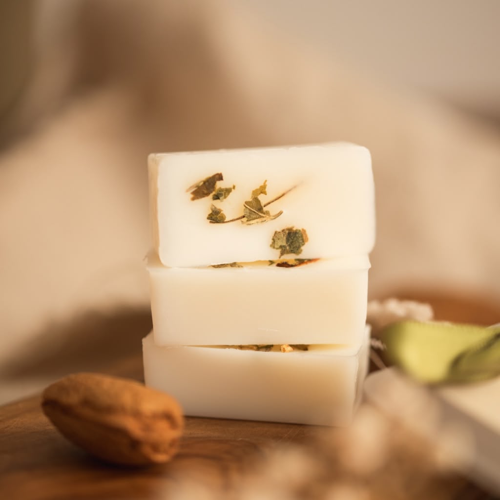 Three stacked white handmade wax melt bars with dried botanical inclusions, displayed on a wooden surface with a soft, warm background.