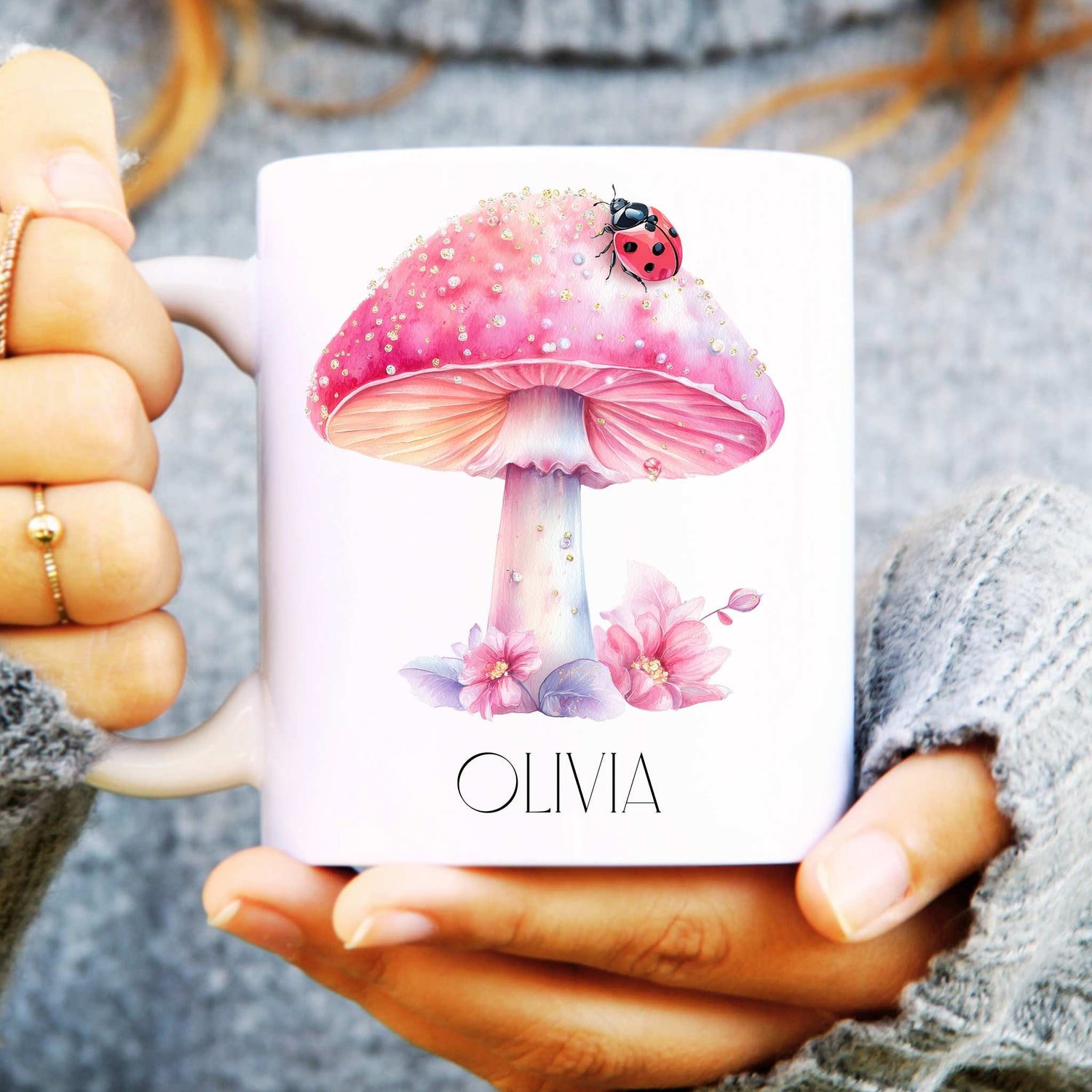 Person holding a mug with a pink mushroom and ladybird design and the name 'OLIVIA'.