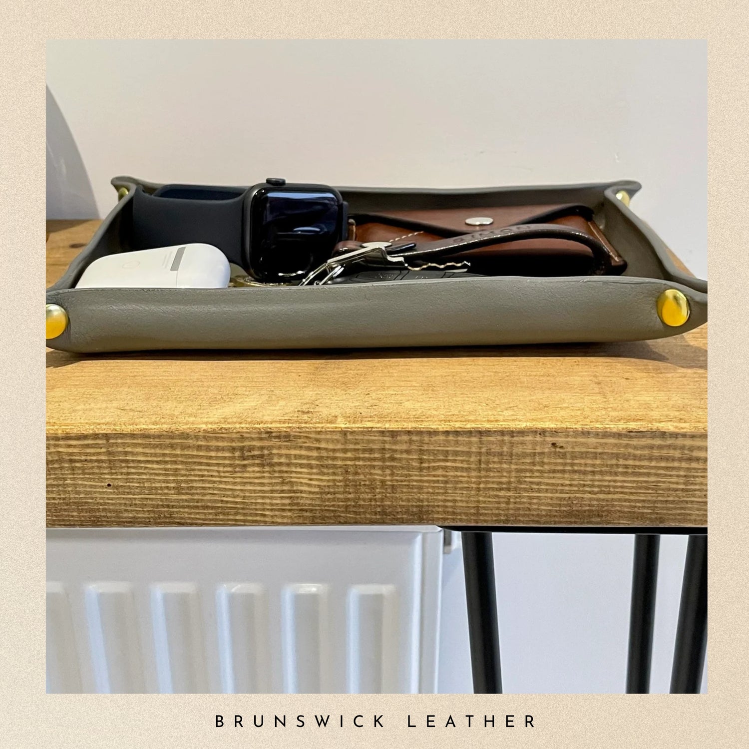 Gray leather tray with small items on a wooden surface, branded 'Brunswick Leather'.