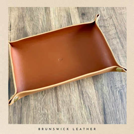 Brown leather tray with gold accents on a wooden surface, branded 'Brunswick Leather'.