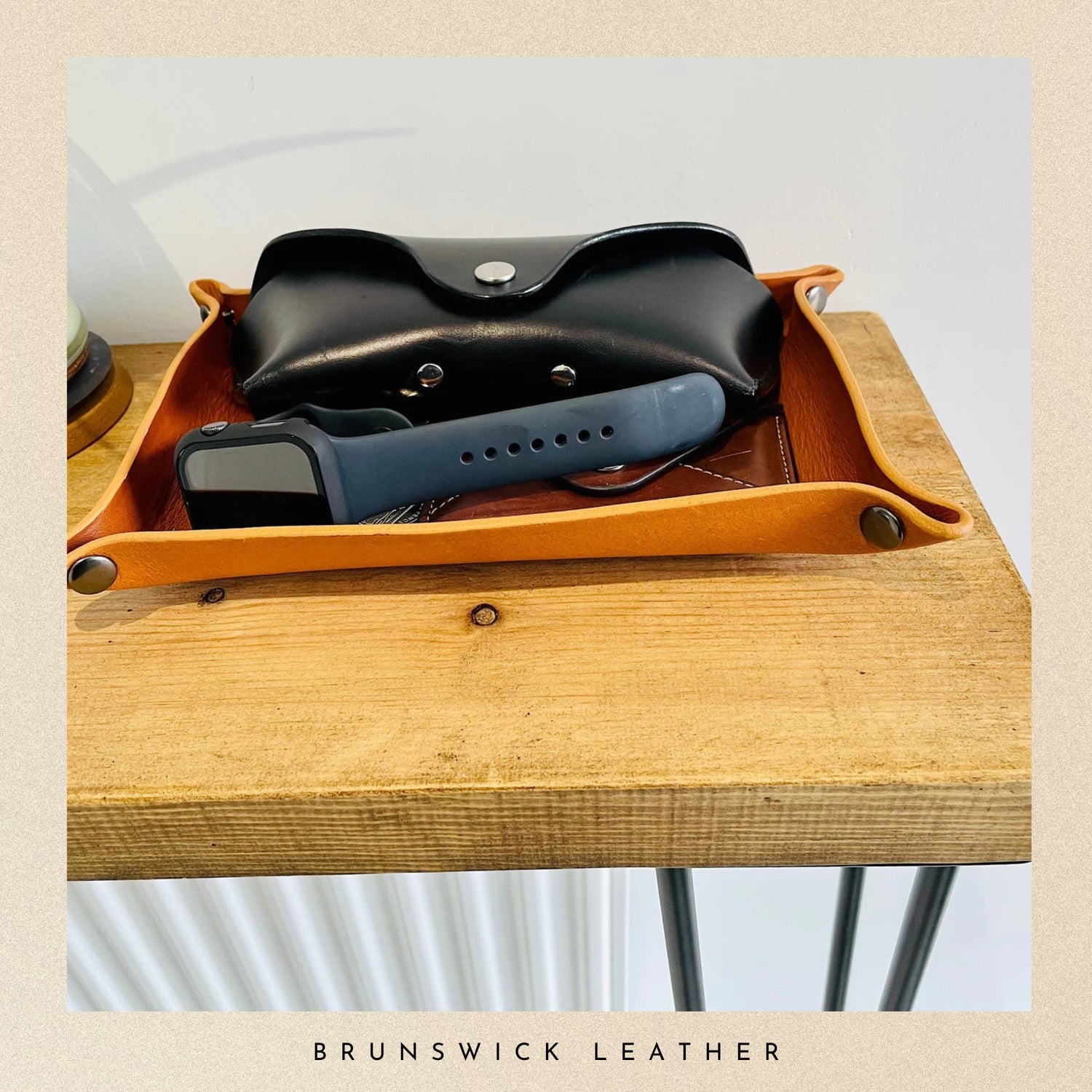 Leather tray with a black pouch and blue device on a wooden surface, branded 'Brunswick Leather'.