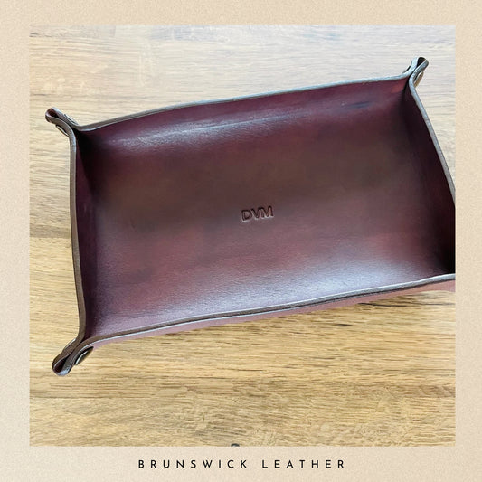 Brown leather tray with 'DVM' branding on a wooden surface, branded 'Brunswick Leather'.