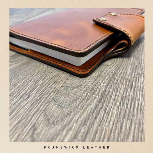 Brown leather notebook on a wooden surface with 'Brunswick Leather' branding.