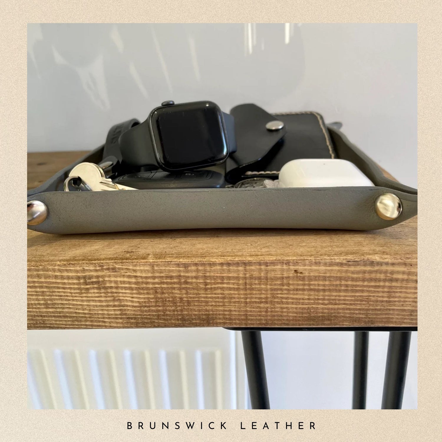 Grey leather tray with a watch on a wooden surface, branded 'Brunswick Leather'.