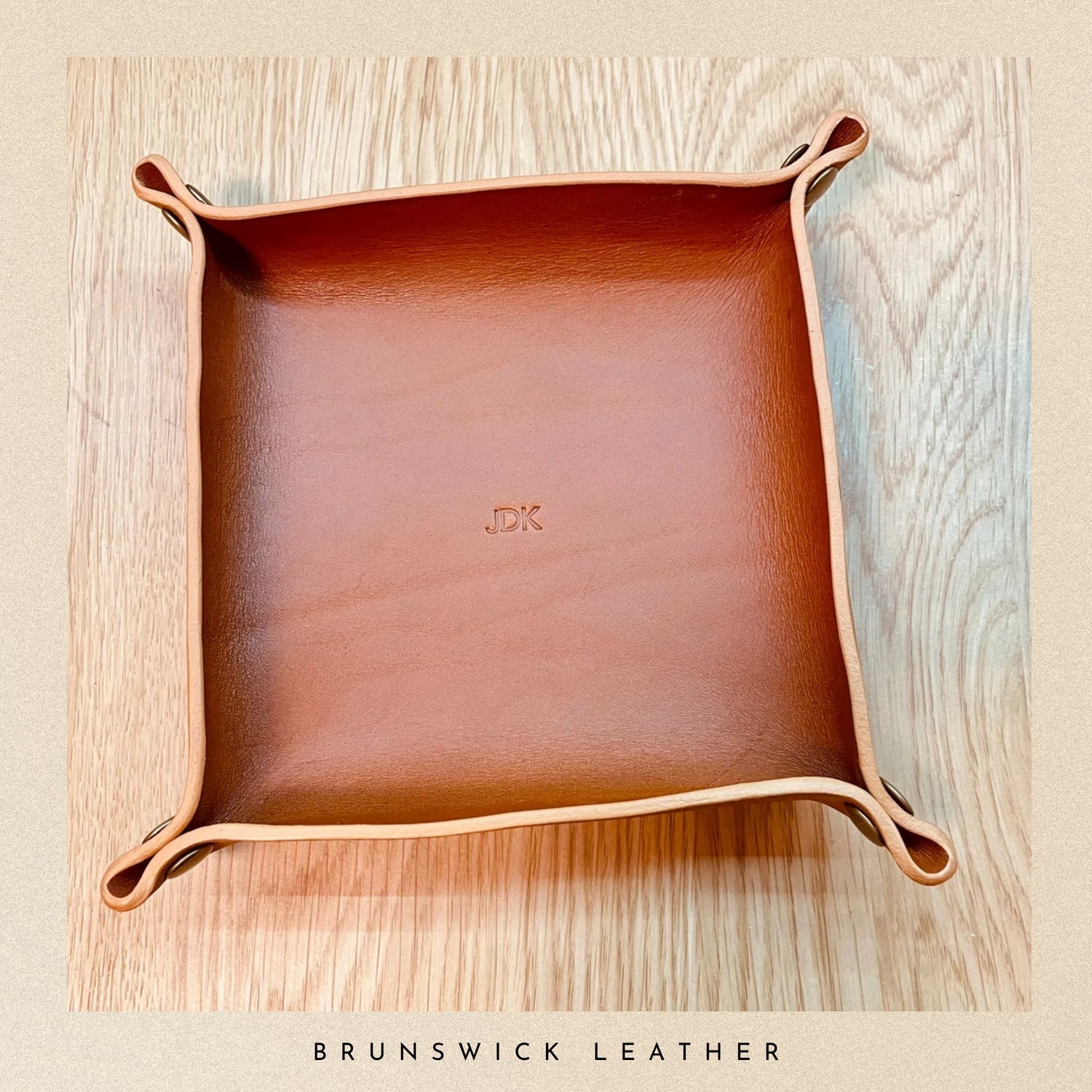 Brown leather tray with 'JK' initials on a wooden surface, branded 'Brunswick Leather'.
