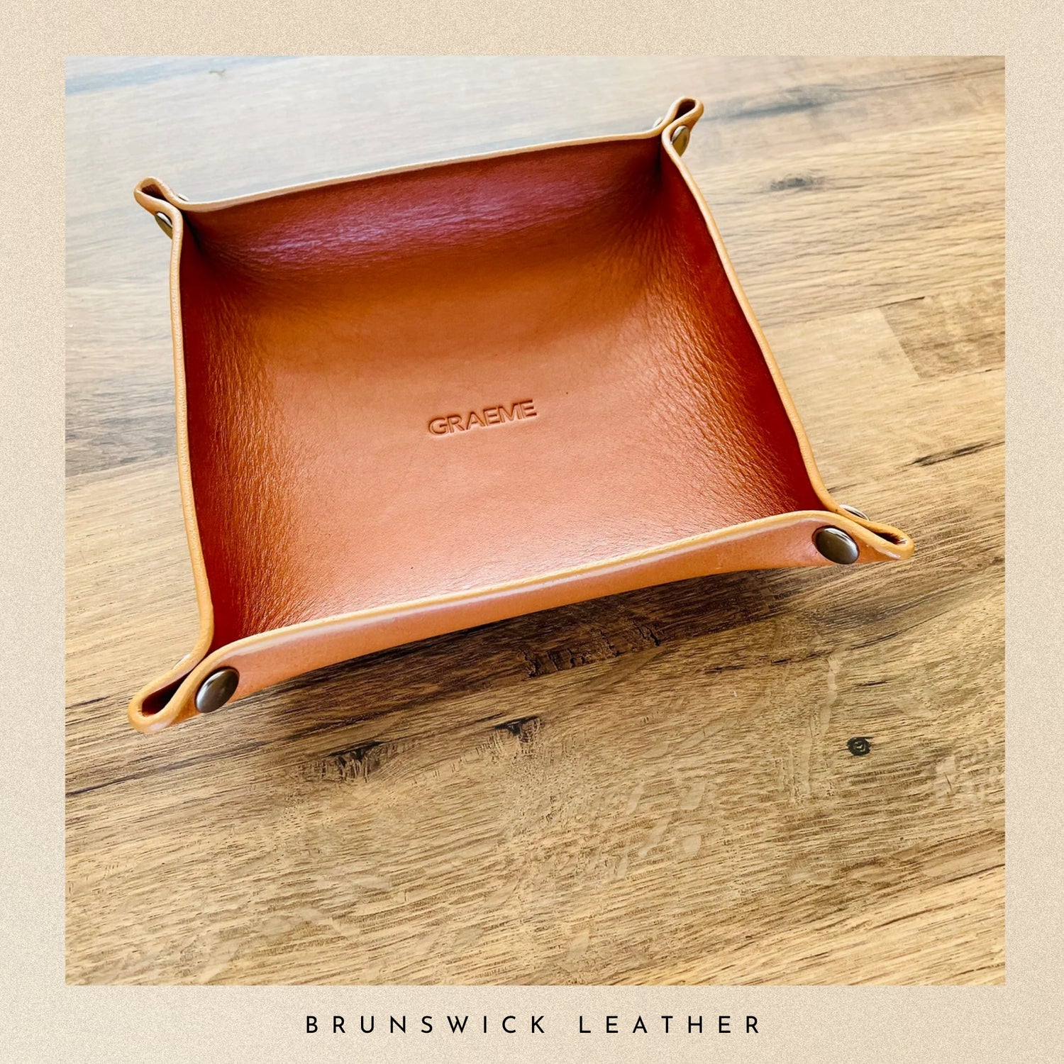 Brown leather tray with 'Brunswick Leather' branding on a wooden surface