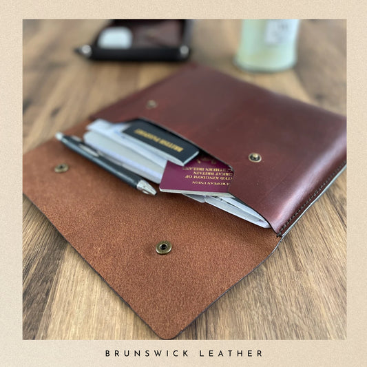 Brown leather wallet with pen and cards on a wooden surface, branded 'Brunswick Leather'.