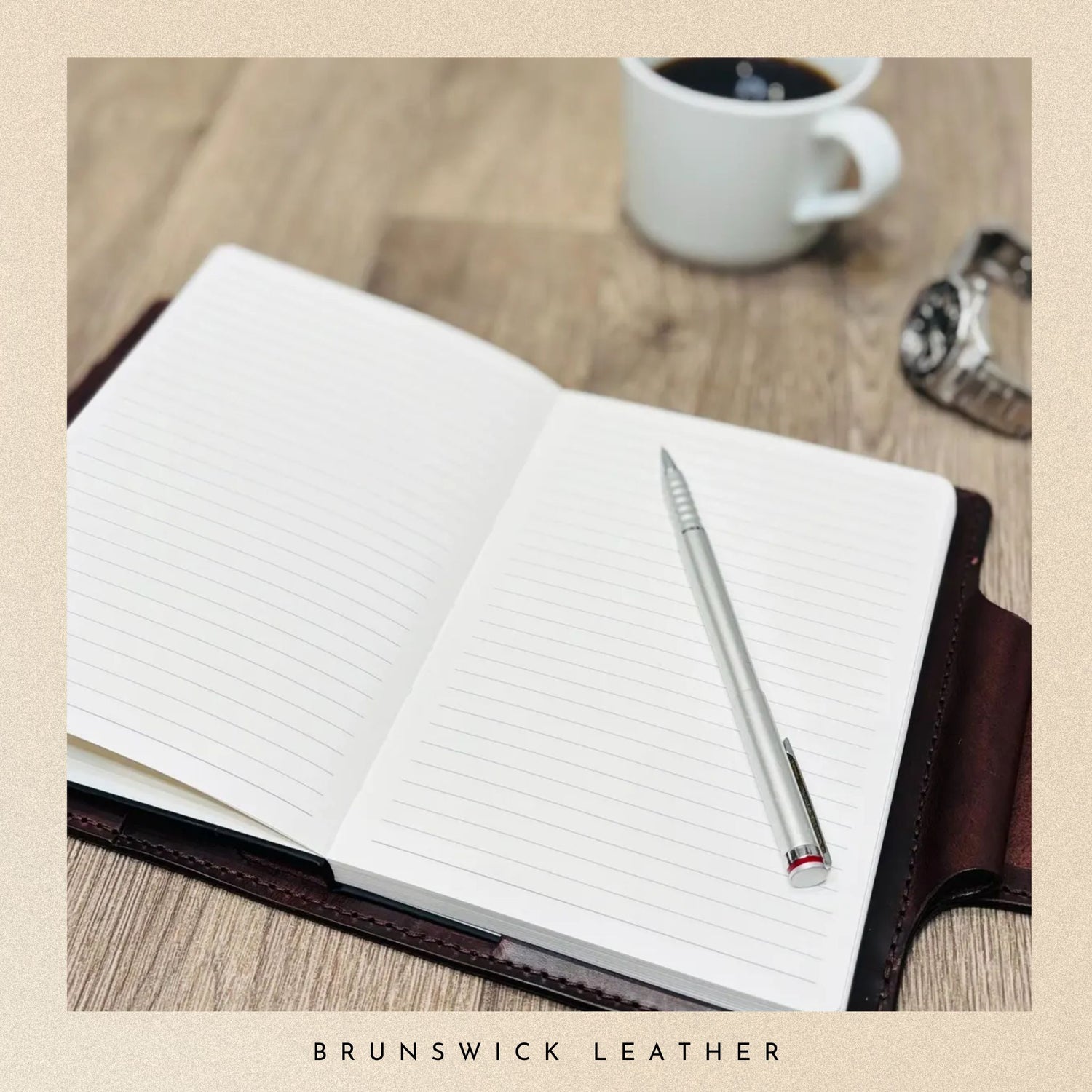 Open notebook with a pen and coffee cup on a wooden surface, branded 'Brunswick Leather'.