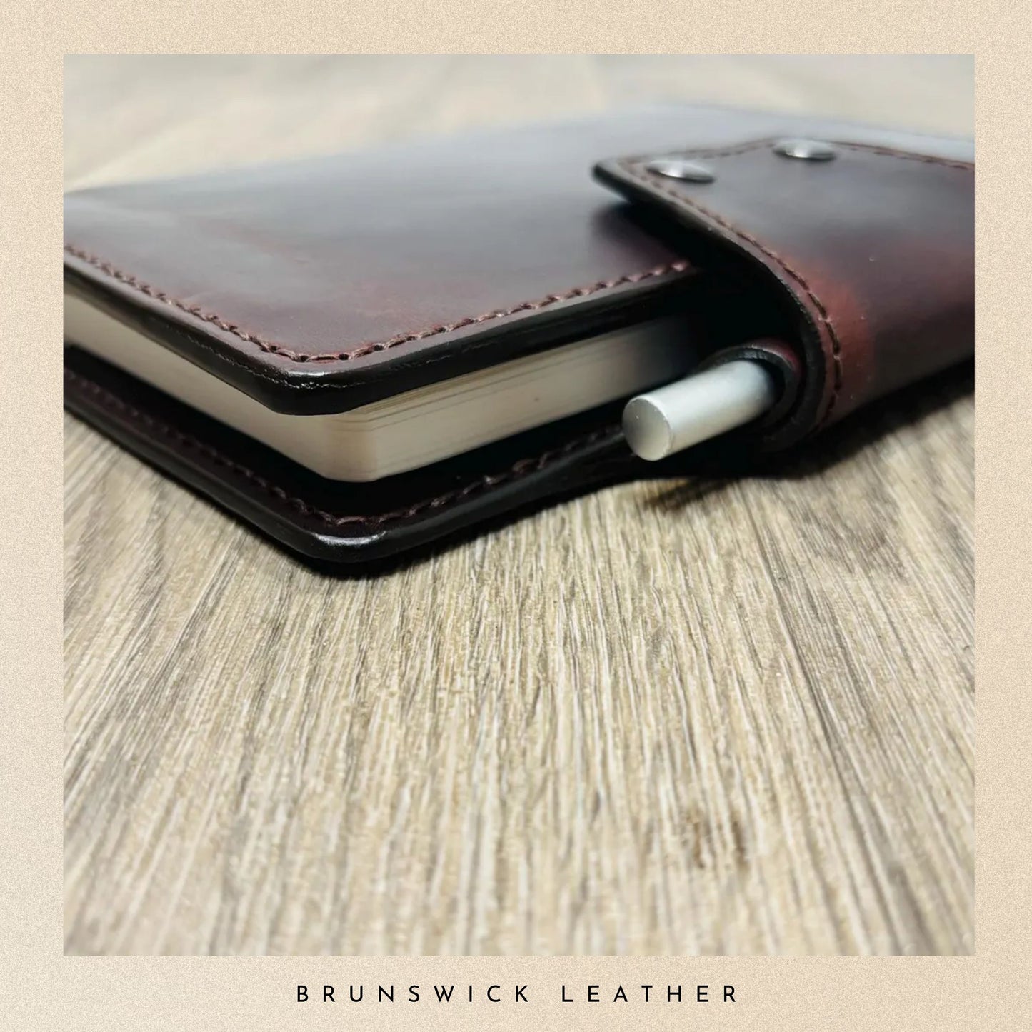 Brown leather notebook with a pen on a wooden surface, branded 'Brunswick Leather'.