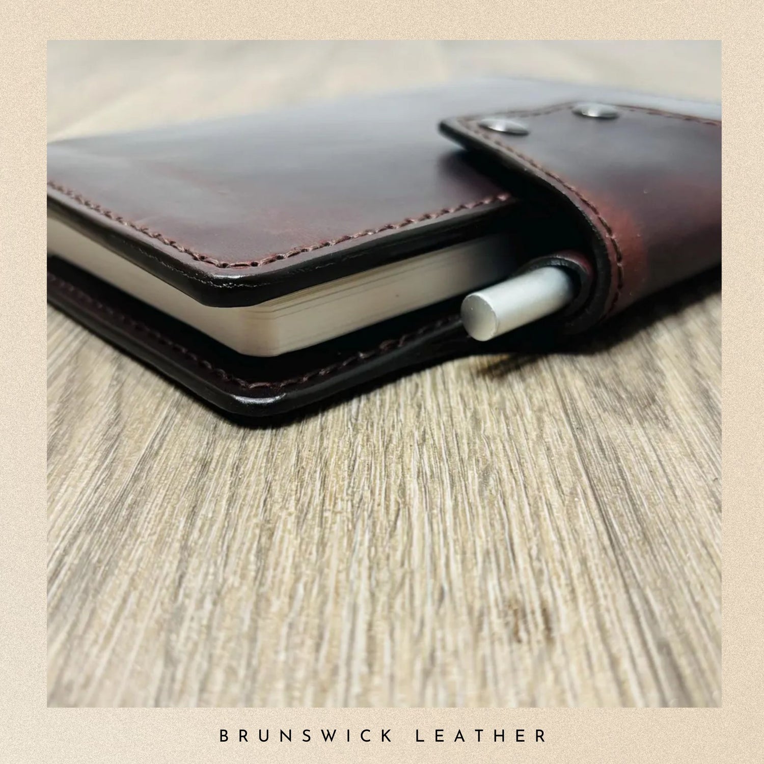 Brown leather notebook with a pen on a wooden surface, branded 'Brunswick Leather'.