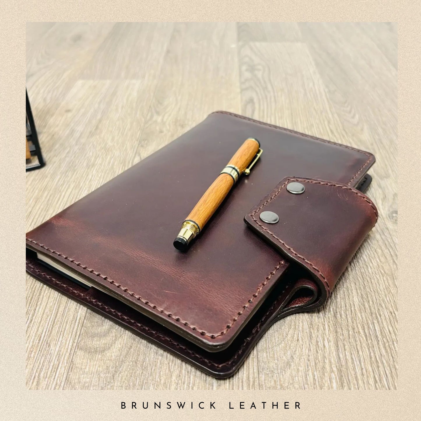 Brown leather notebook with a pen on a wooden surface, branded 'Brunswick Leather'.