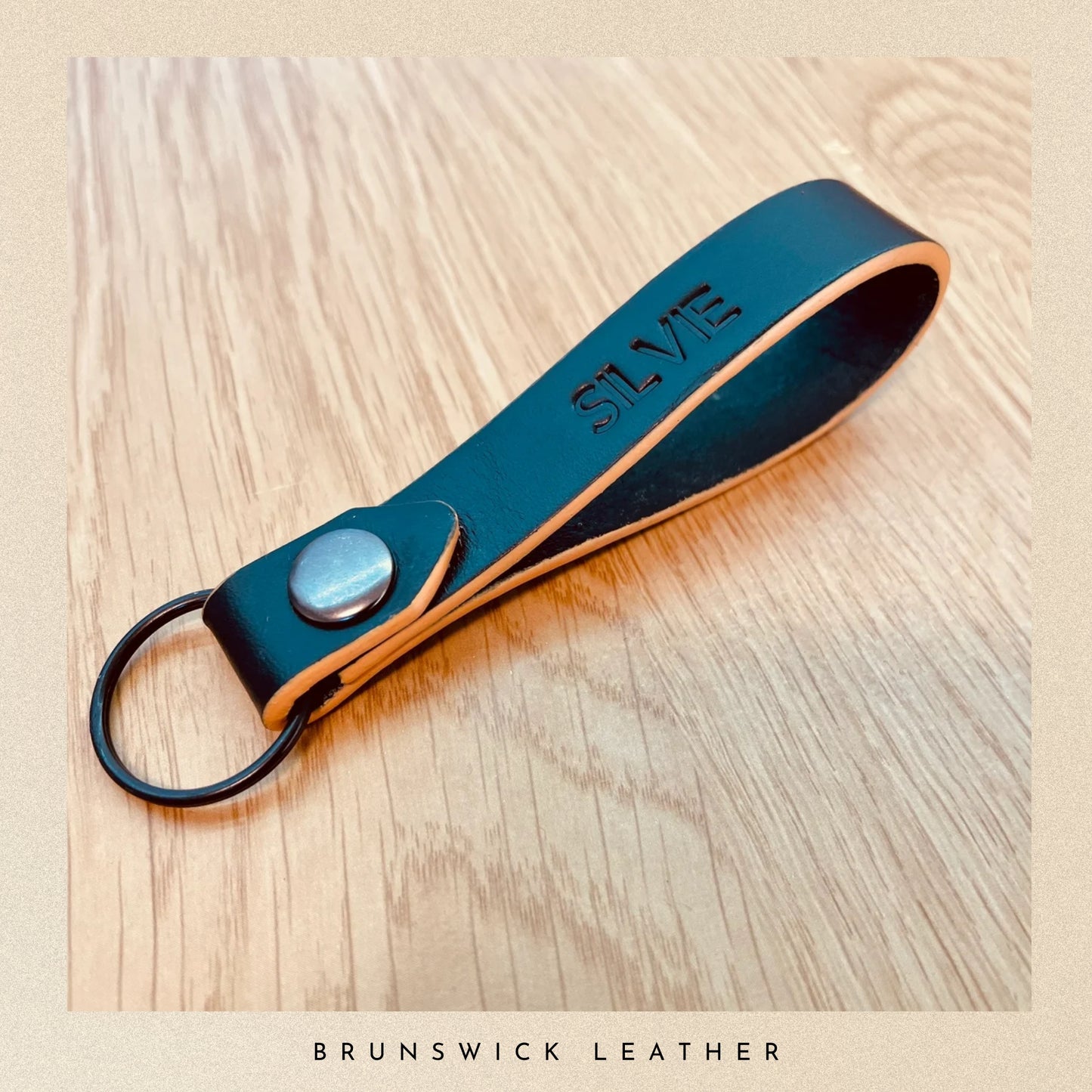 Black leather keychain with 'SILVIE' branding on a wooden surface, featuring 'Brunswick Leather' text.