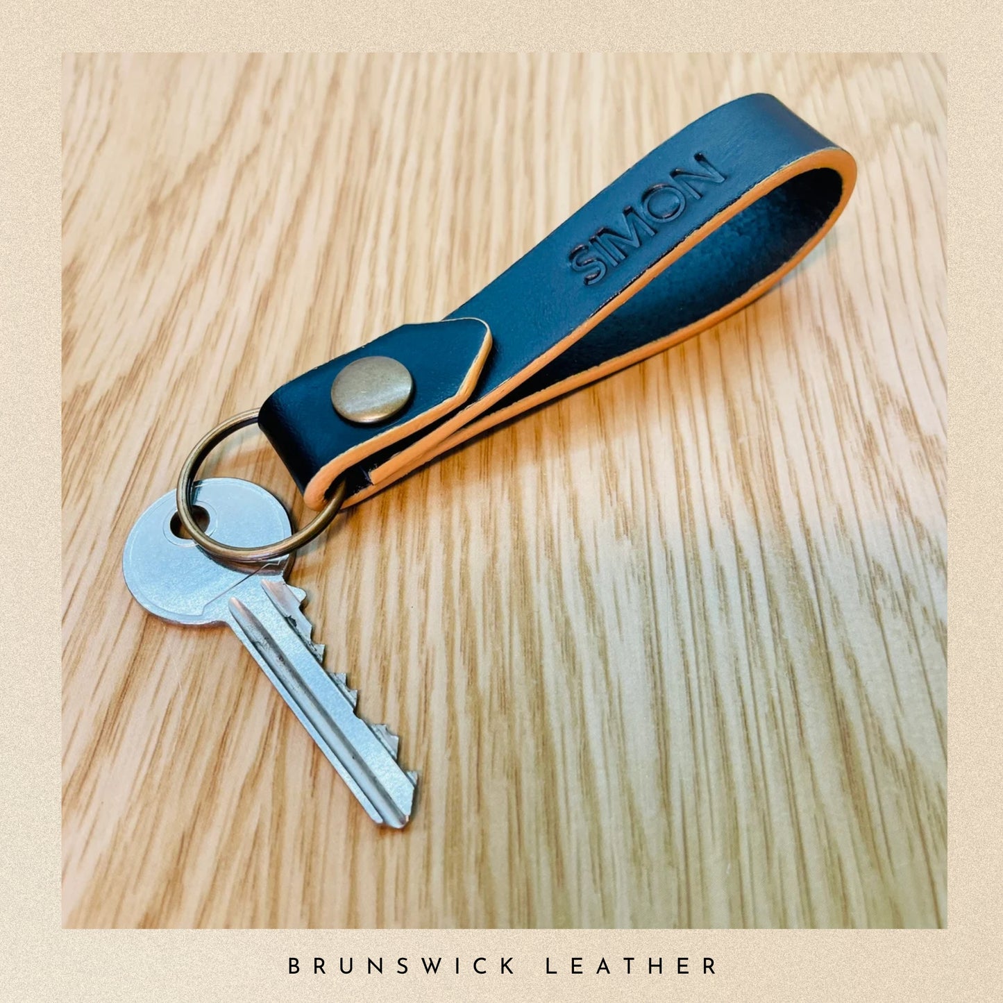 Black leather keychain with keys on a wooden surface, branded 'Brunswick Leather'.