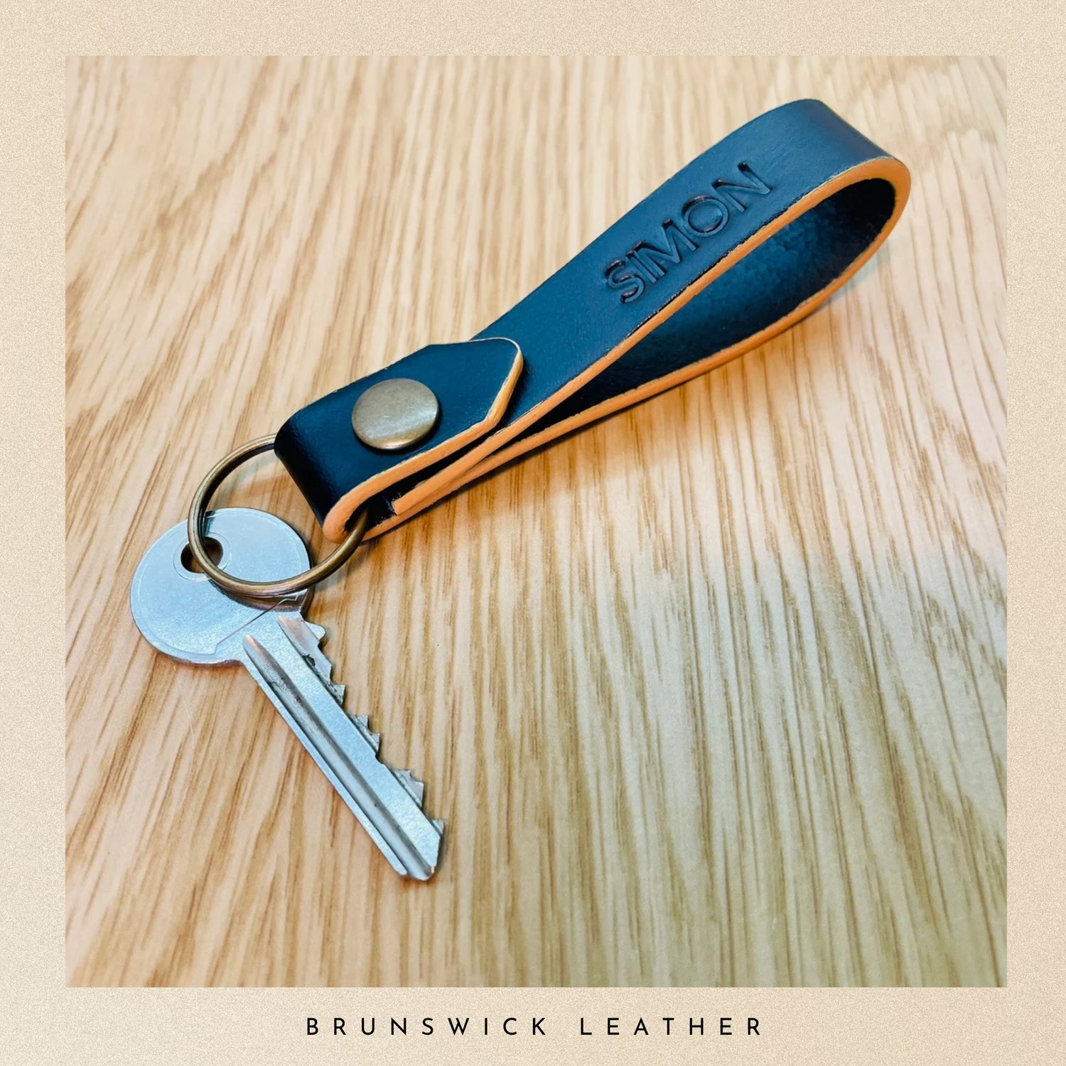 Black leather keychain with keys on a wooden surface, branded 'Brunswick Leather'.
