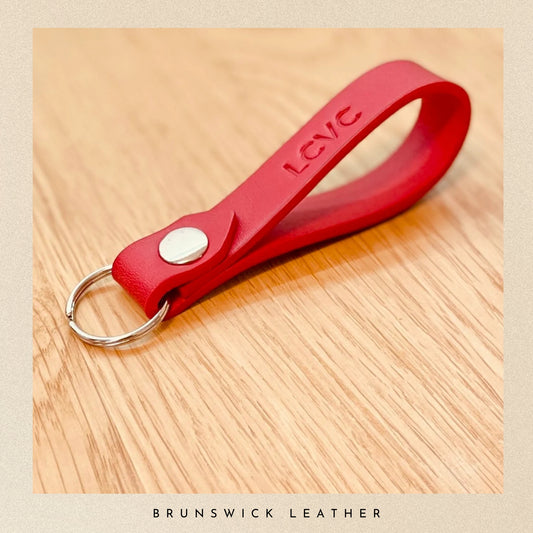 Red leather keychain with 'LCVC' branding on a wooden surface, featuring 'Brunswick Leather' text.