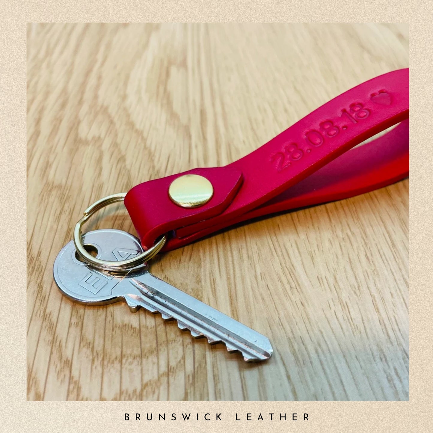 Red leather keychain with keys on a wooden surface, branded 'Brunswick Leather'.