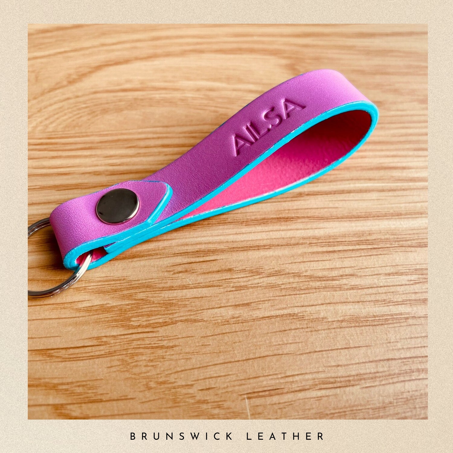 Pink and blue key fob with 'Ailsa' branding on a wooden surface, featuring 'Brunswick Leather' text.