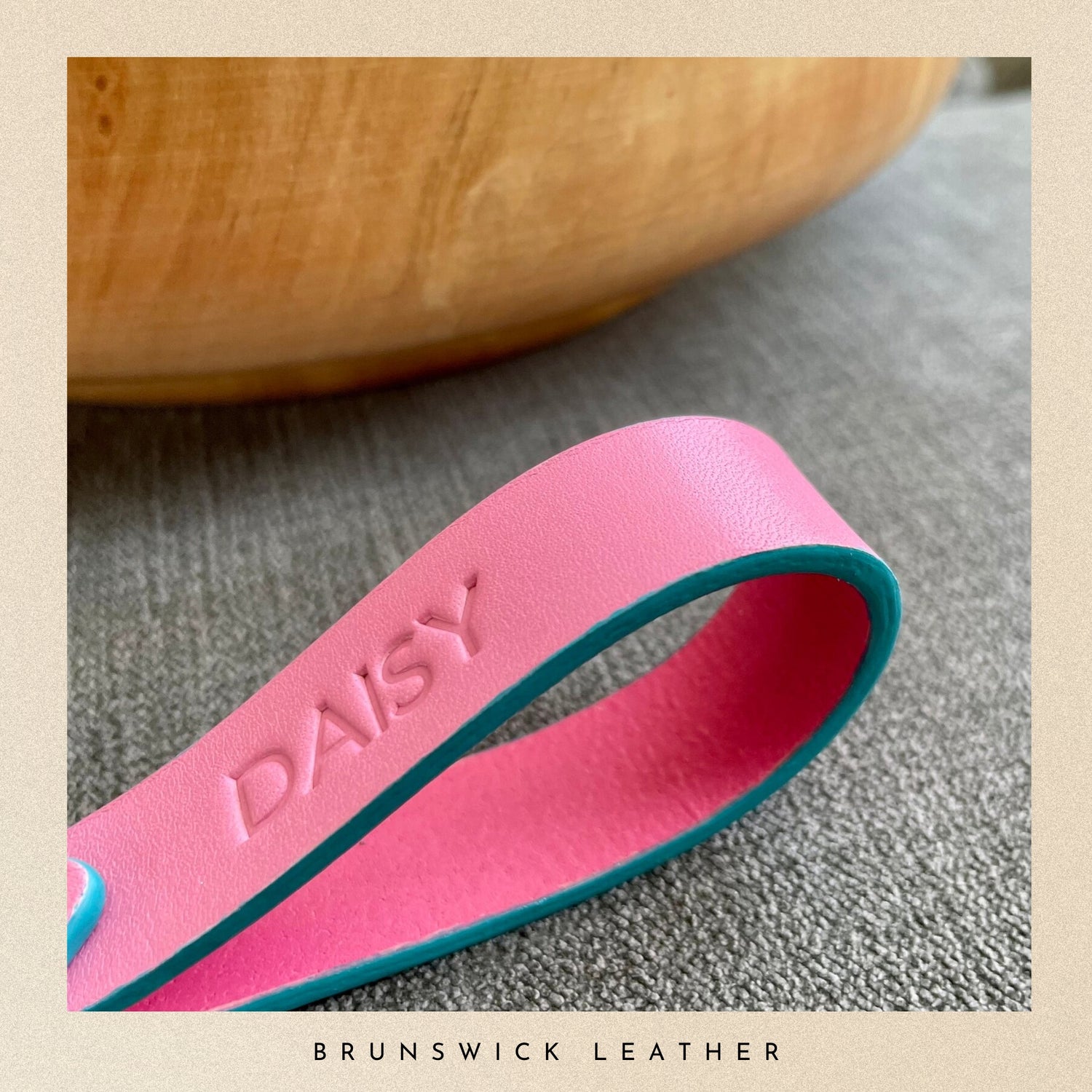 Pink leather strap with 'DAISY' embossed on it, lying on a textured surface.