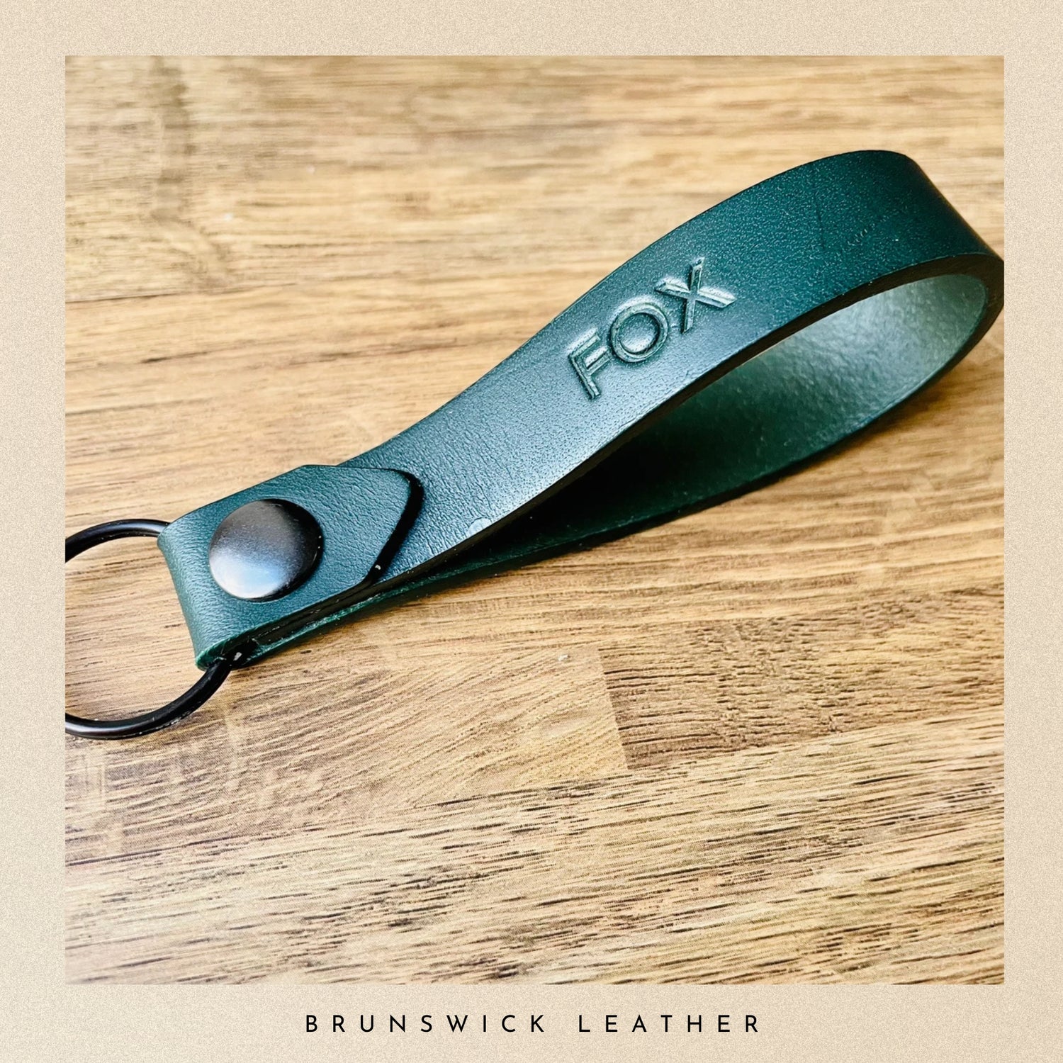 Green leather keychain with 'FOX' branding on a wooden surface, featuring 'Brunswick Leather' text.