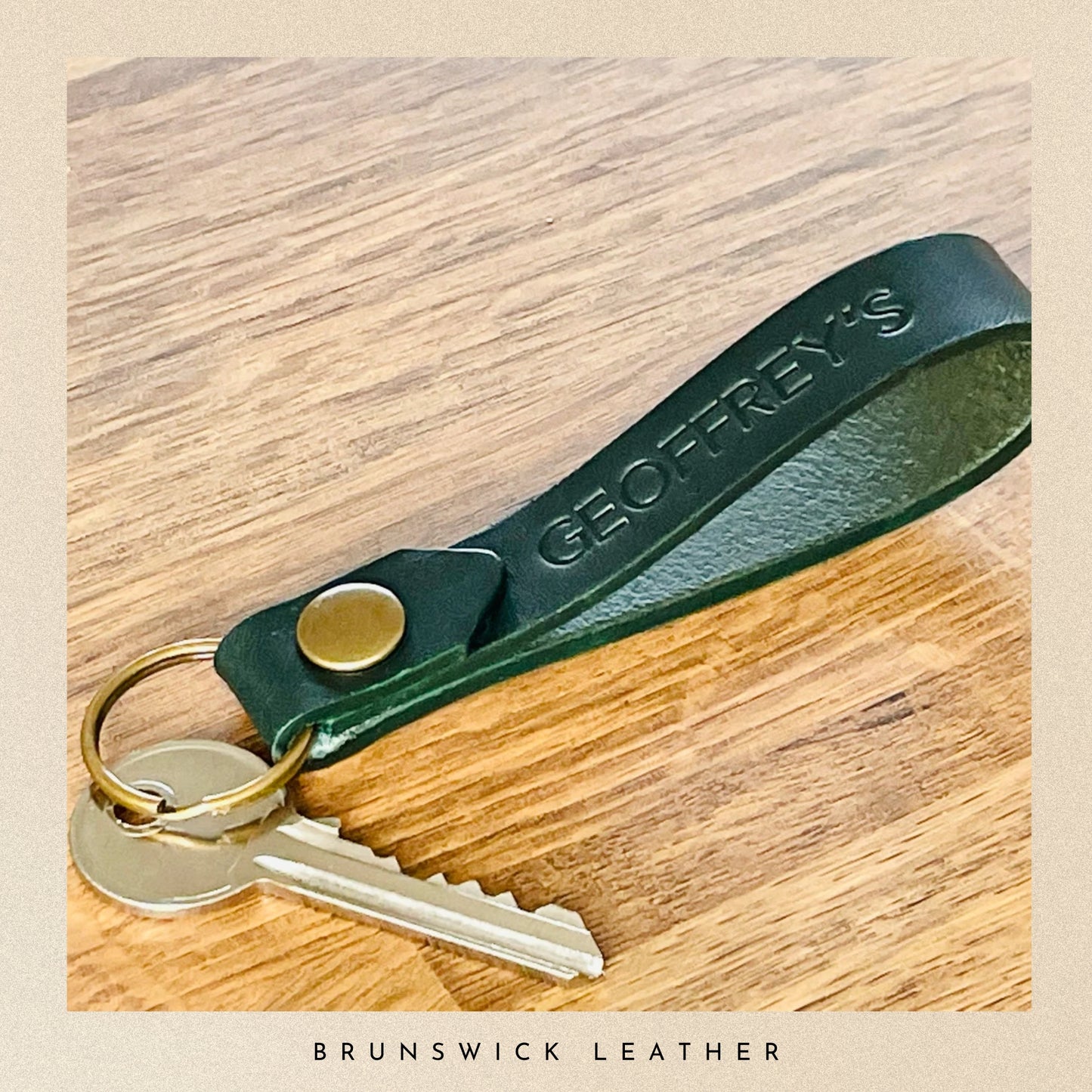 Green leather keychain with keys on a wooden surface, featuring 'Geoffrey's Brunswick Leather' branding.