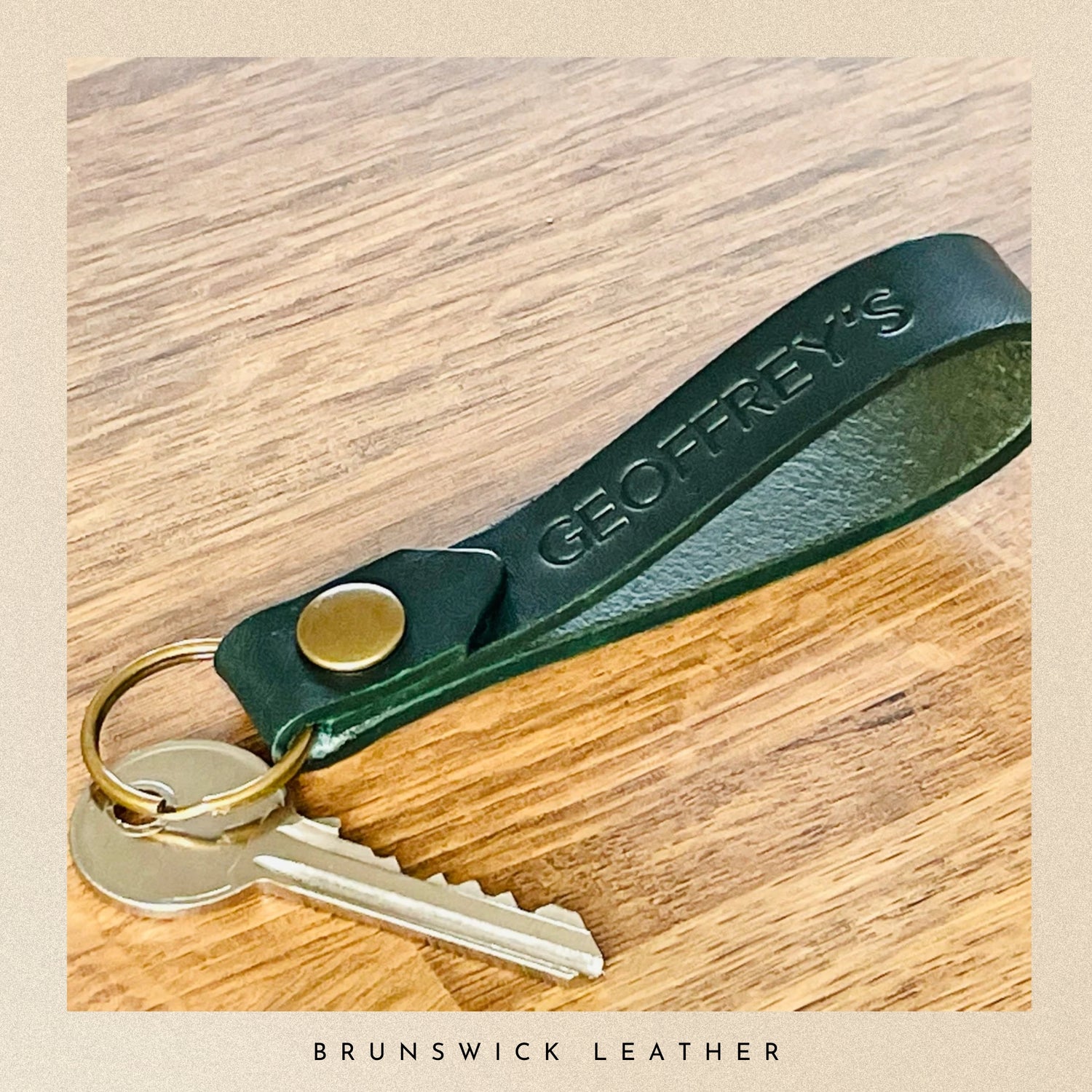 Green leather keychain with keys on a wooden surface, featuring 'Geoffrey's Brunswick Leather' branding.
