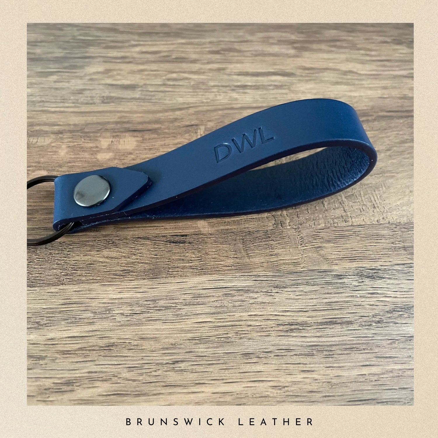 Blue leather key strap with 'DWL' engraving on a wooden surface, branded 'Brunswick Leather'.