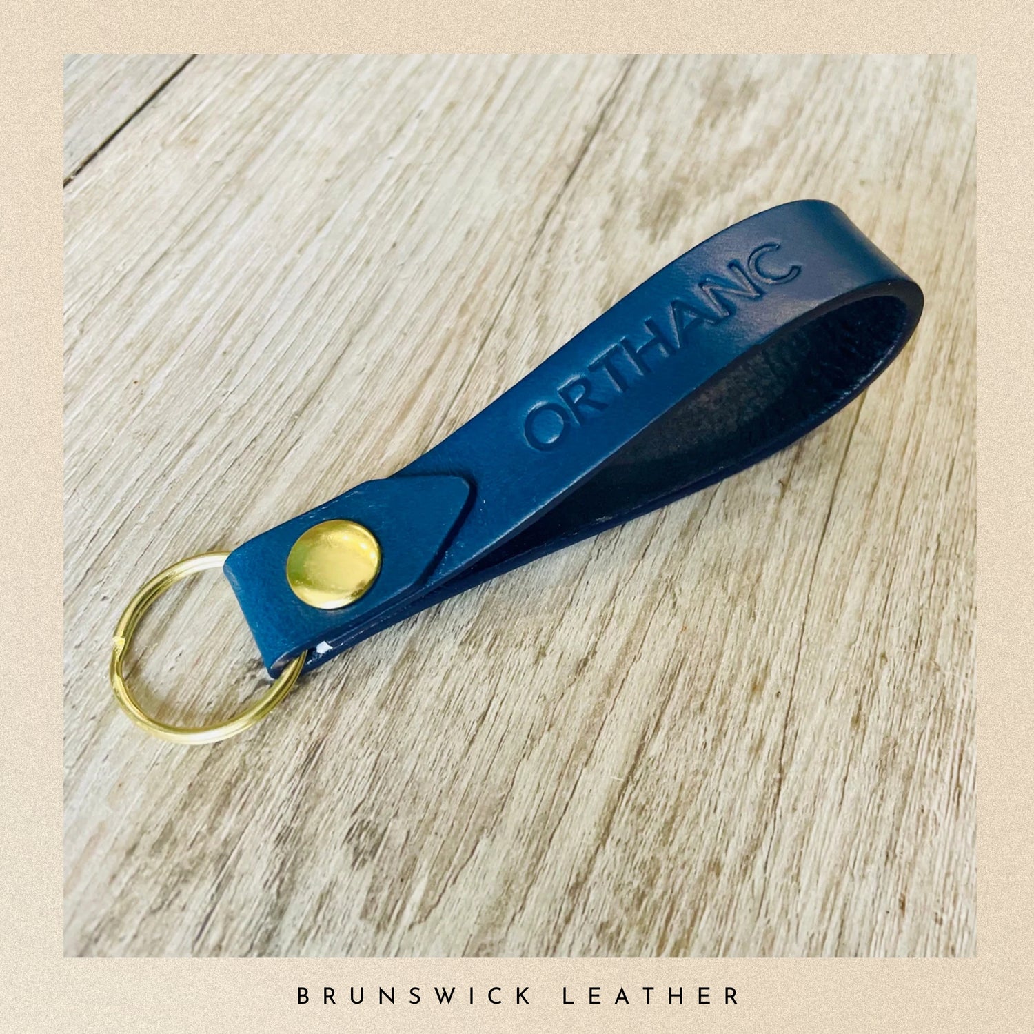 Blue leather keychain with gold accent on a wooden surface, branded 'Brunswick Leather'.
