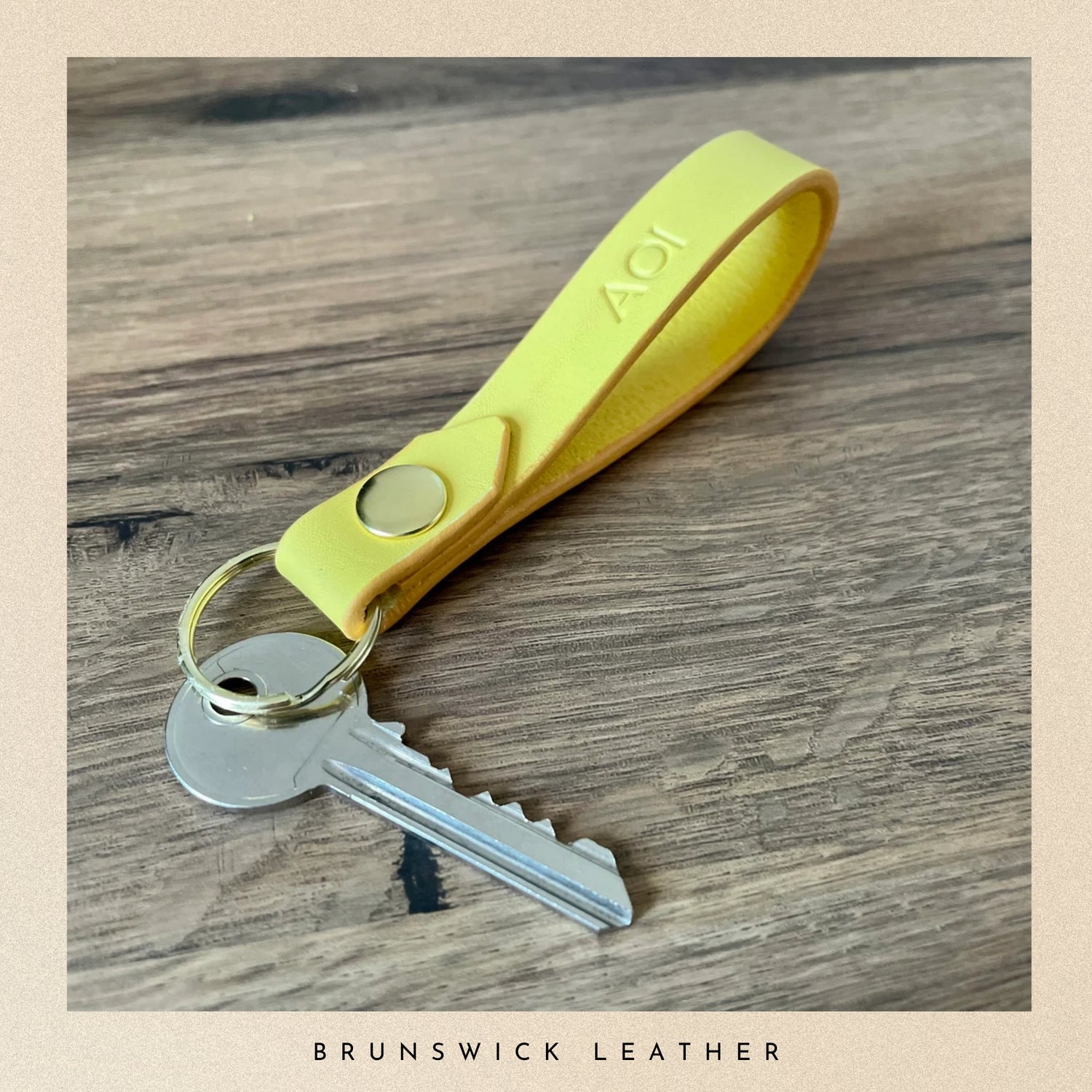 Yellow keychain with a key on a wooden surface, branded 'Brunswick Leather'.