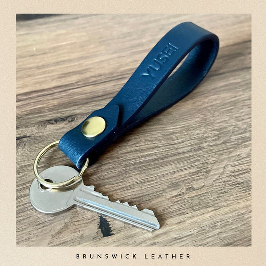 Blue leather keychain with gold accent on a wooden surface, branded 'Yusef'.