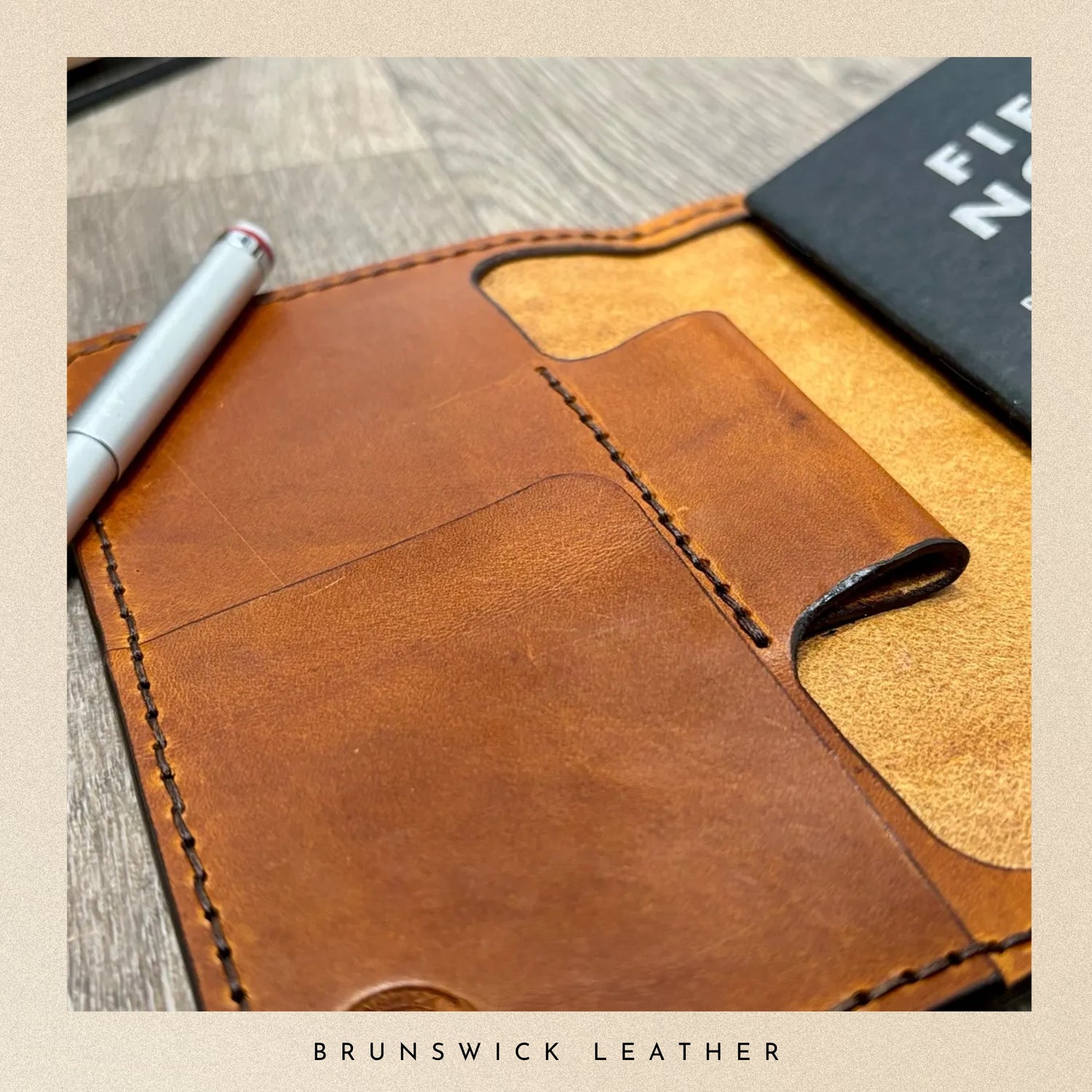 Brown leather notebook with a pen on a wooden surface, branded 'Brunswick Leather'.