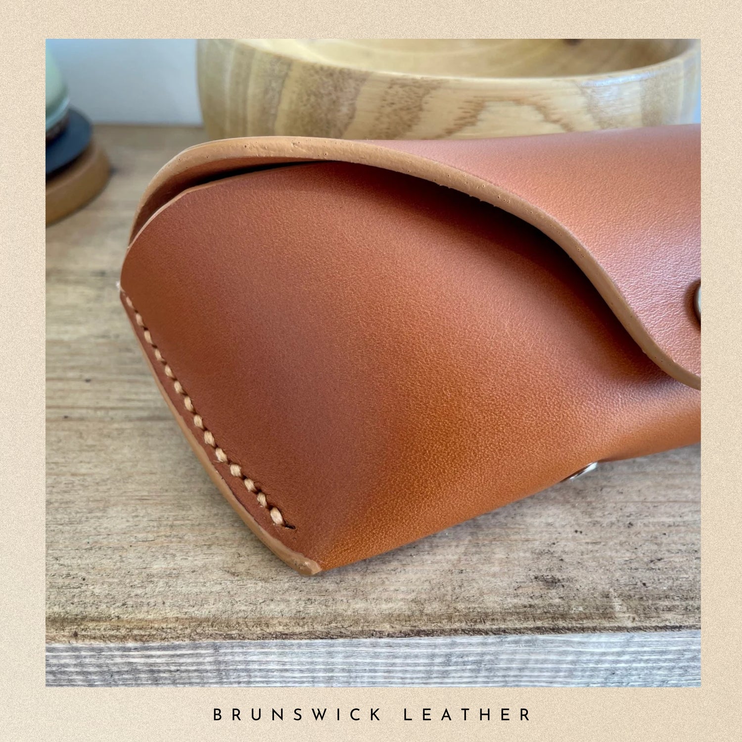 Close-up of a brown leather product with visible stitching on a wooden surface, branded 'Brunswick Leather'.