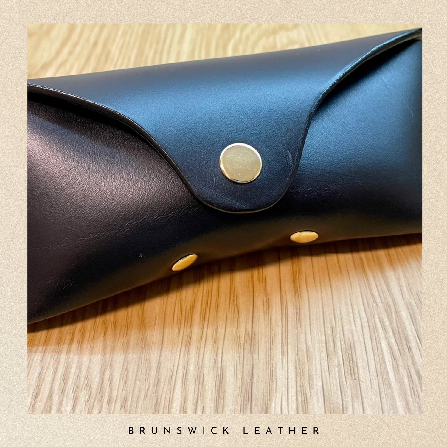 Blue leather case with gold studs on a wooden surface, branded 'Brunswick Leather'.