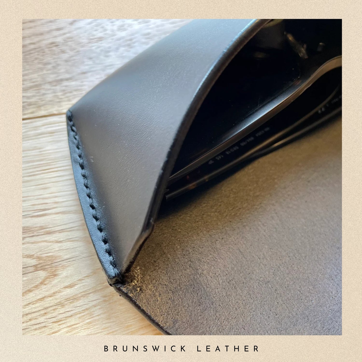 Close-up of a black leather wallet on a wooden surface with 'Brunswick Leather' branding.