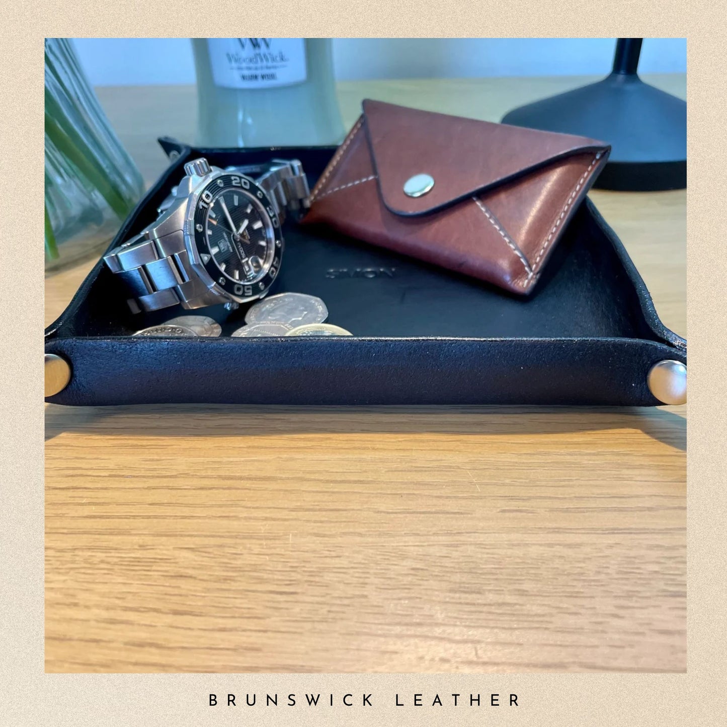 Leather tray with a watch, coin pouch, and coins on a wooden surface with 'Brunswick Leather' branding.