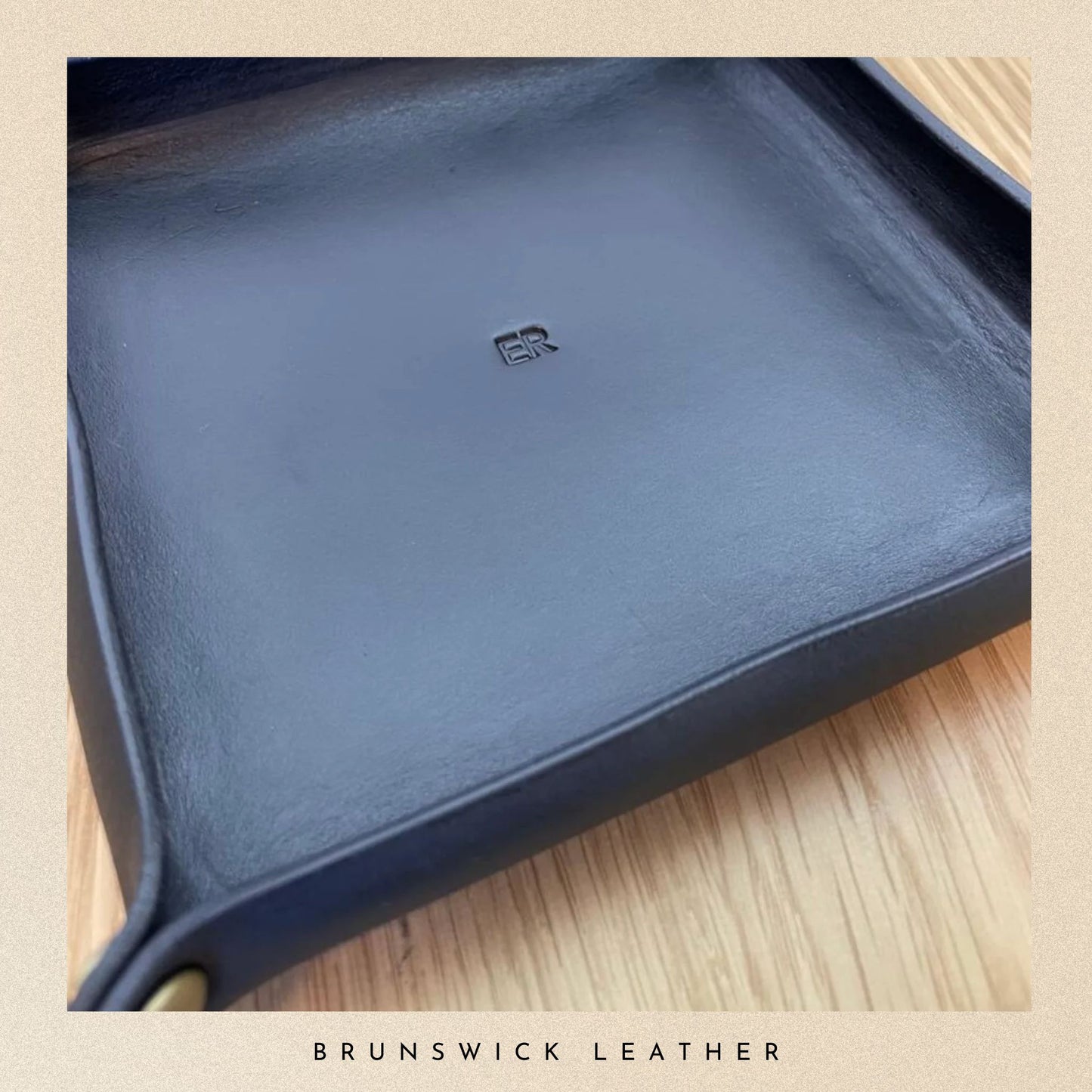 Blue leather tray with a visible brand logo on a wooden surface, branded 'Brunswick Leather'.