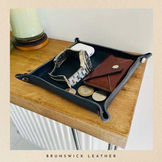 Black leather tray with accessories on a wooden surface, featuring the brand 'Brunswick Leather'.