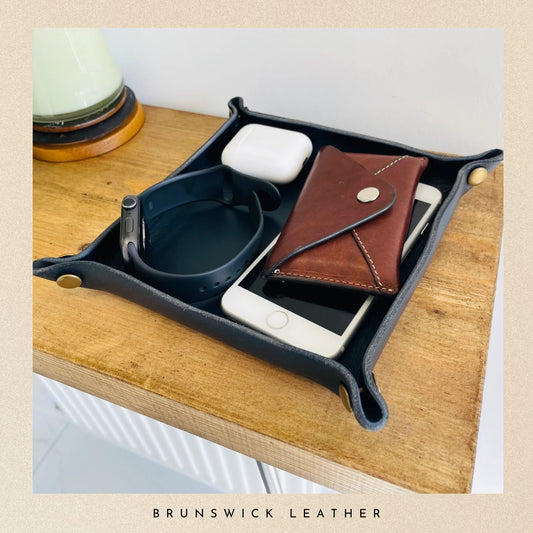 Organizer tray with phone, wallet, and other items on a wooden surface, featuring Brunswick Leather branding.