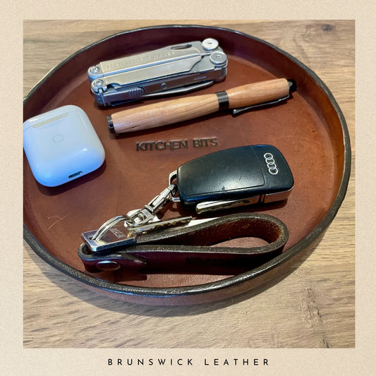 Collection of items including air pods, pen, and car key fob on a leather tray with 'Kitchen Bits' branding.