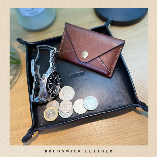 Brown leather wallet and watch on a black leather tray with coins, branded 'Brunswick Leather'.