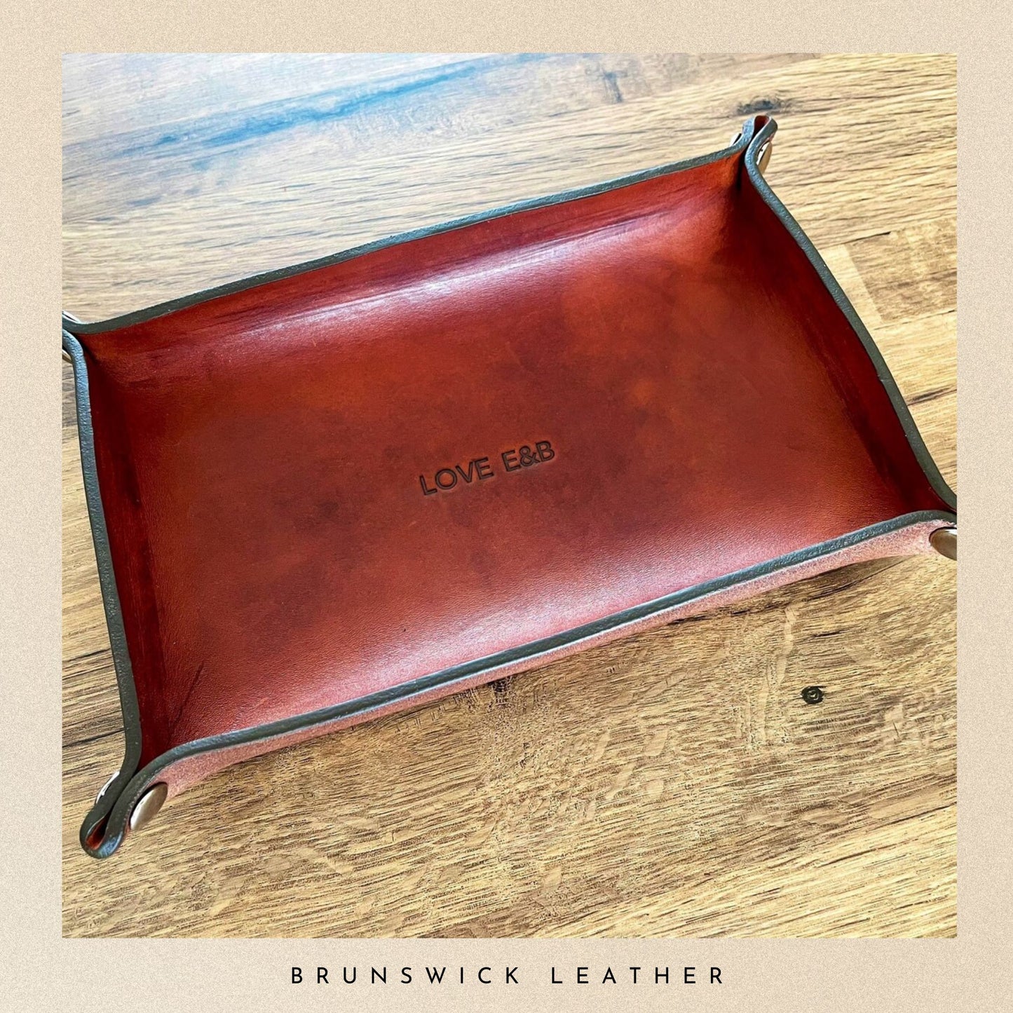 Brown leather tray with 'LOVE & B' branding on a wooden surface, branded 'Brunswick Leather'.
