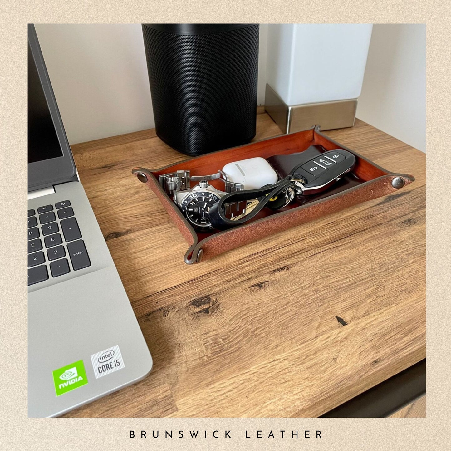 Wooden desk with a laptop, speaker, and decorative tray holding keys and other items on a beige background.