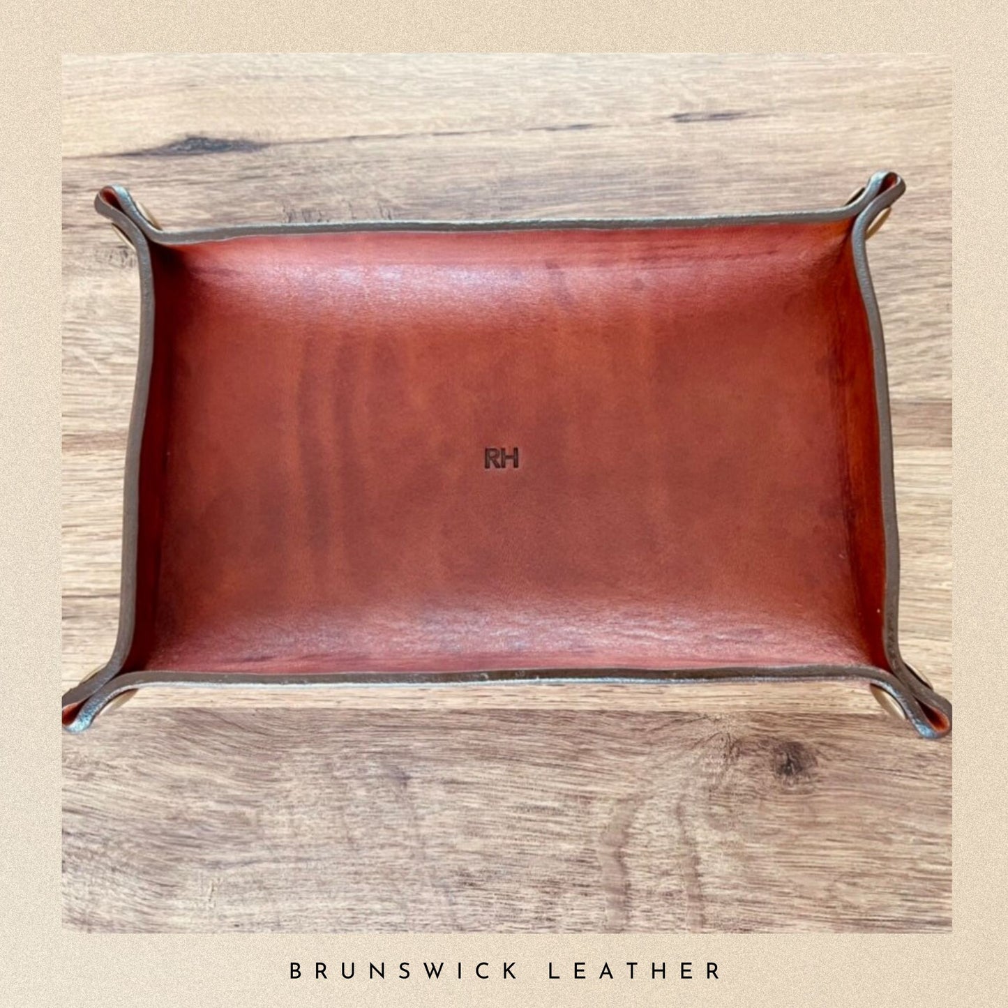 Brown leather tray with metal legs on a wooden surface, branded 'RH'.
