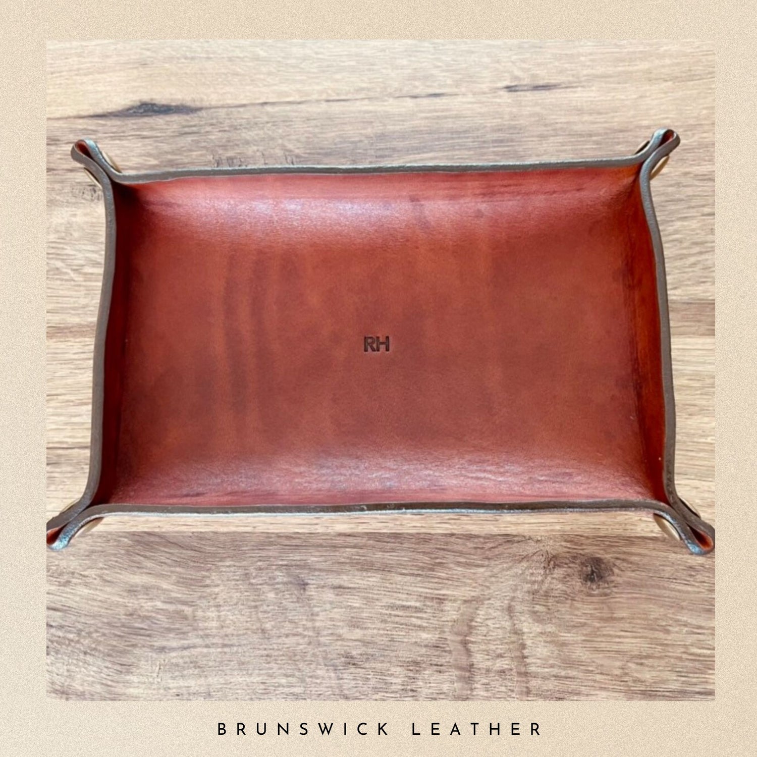 Brown leather tray with metal legs on a wooden surface, branded 'RH'.
