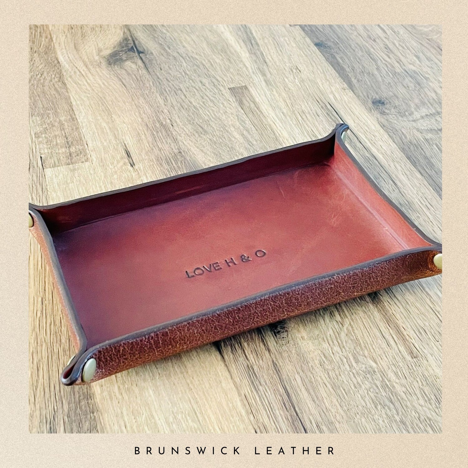 Brown leather tray with 'LOVE H & O' engraving on a wooden surface, branded 'Brunswick Leather'.