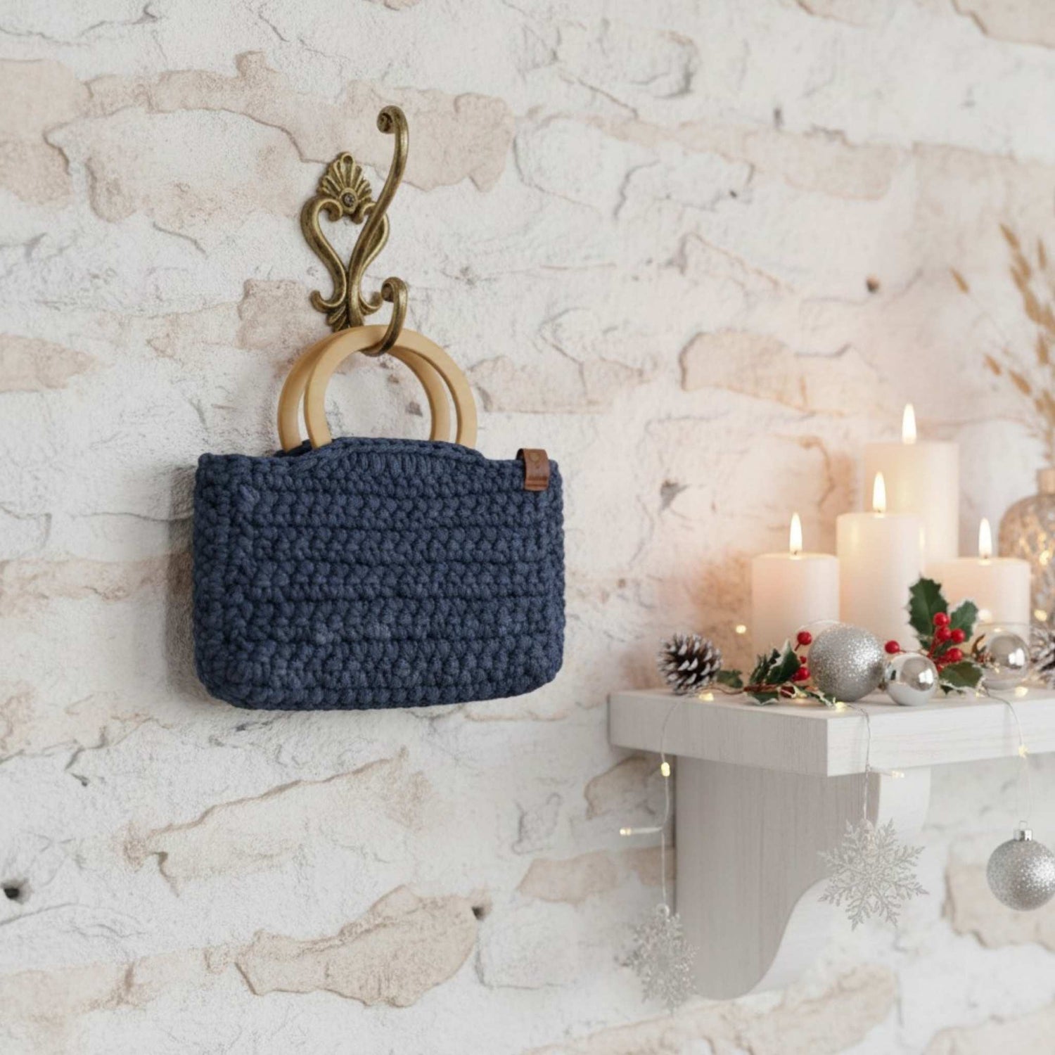 Blue crocheted bag hanging on a decorative wall hook with candles and Christmas decorations in the background.