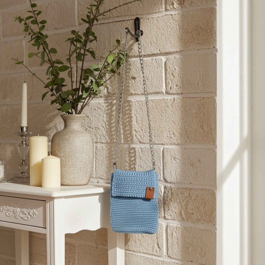 Light blue woven bag hanging on a brick wall with a vase and candles on a table.
