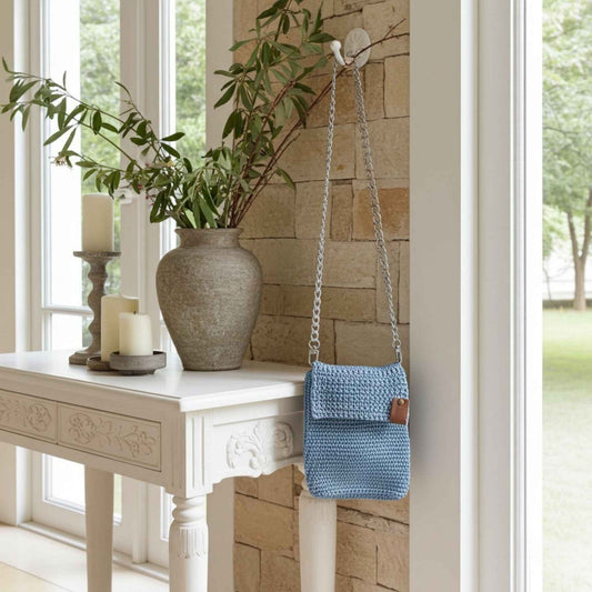 Blue crochet bag on a white table with a stone wall and window in the background