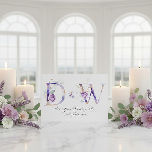 Decorative setup with candles, flowers, and a card with initials and date on a marble surface.